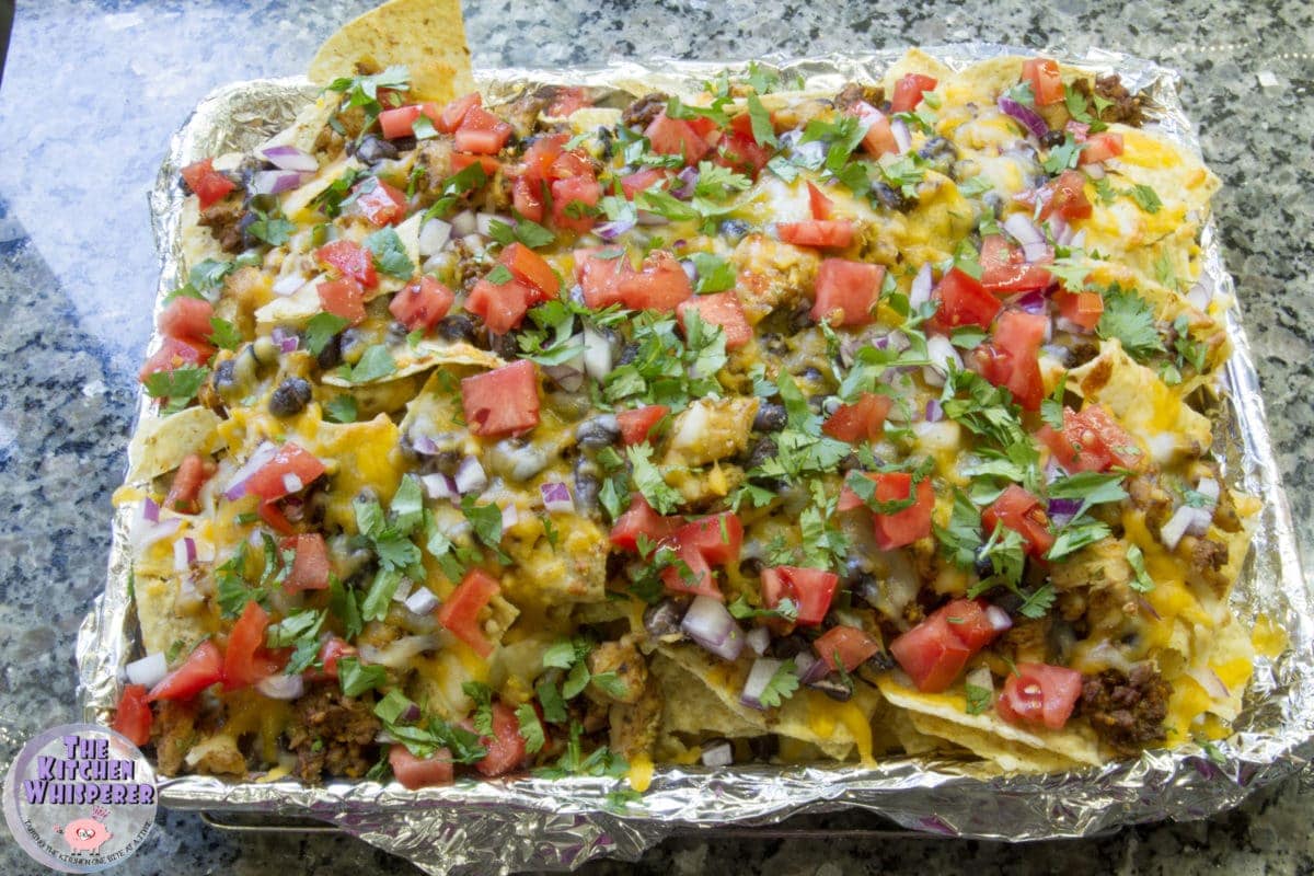Loaded Sheetpan Nachos for a crowd! Meats, beans, cheese, veggies, cilantro and salsa make up this crowd-please nacho dish!