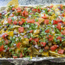 Loaded Sheetpan Nachos for a crowd! Meats, beans, cheese, veggies, cilantro and salsa make up this crowd-please nacho dish!