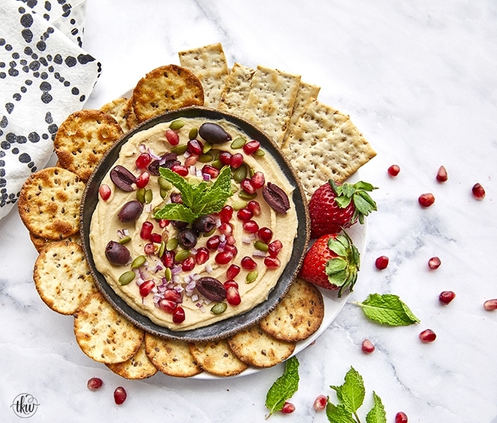 This Mediterranean Hummus Bowl is garnished with Mediterranean Hummus Bowl, toasted pepitas, arils, red onions, and a kiss of mint for a tasty vegetarian snack or lunch!