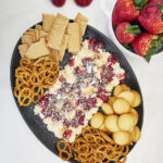 Cheesecake for a crowd has never been easier! Creamy no-bake cheesecake topped with strawberry compote, graham crumbles, & white chocolate! Serve with cookies, pretzels & crackers! Ultimate No-Bake Strawberry Cheesecake Party Platter, strawberry compote, dessert board, dessert grazing platter, dessert for two, table dessert, cheesecake dip