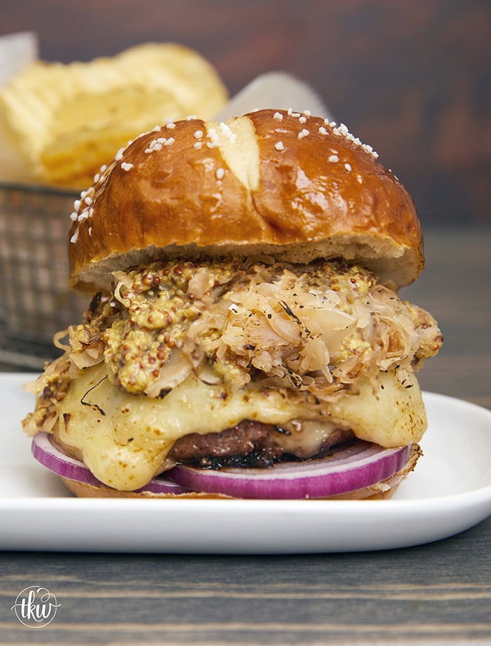 Prepare to take your taste buds on a flavor-packed journey of a perfectly grilled bratwurst burger stuffed with sauerkraut and gooey Swiss cheese. A slice of red onion, crispy sauerkraut, and whole-grain mustard on a pretzel bun will make this your new favorite burger! The Best Grilled German Bratwurst Burgers Stuffed With Cheese & Sauerkraut, grilled German bratwurst, juicy Lucy German burgers, Oktoberfest burgers, stuffed burgers, pork burgers, sausage burgers, grilled burgers