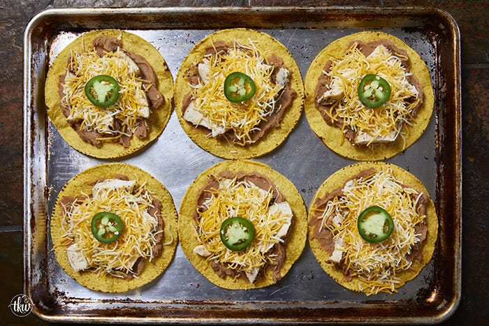 The crunch you've been craving! These Loaded Chicken and Bean Tostadas feature golden-baked shells, seasoned refried beans, juicy chicken, bubbly Mexican cheese, and spicy jalapeños. Finished with a cool sour cream sauce and fresh cilantro for that perfect creamy-meets-crunchy bite. If you love tacos, you have to try this 30-minute twist! #ChickenTostadas #30MinuteMeals #EasyMexicanRecipes #WeeknightDinnerIdeas #BudgetFriendlyCooking