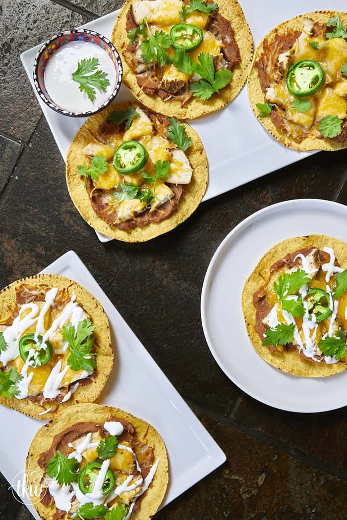 The crunch you've been craving! These Loaded Chicken and Bean Tostadas feature golden-baked shells, seasoned refried beans, juicy chicken, bubbly Mexican cheese, and spicy jalapeños. Finished with a cool sour cream sauce and fresh cilantro for that perfect creamy-meets-crunchy bite. If you love tacos, you have to try this 30-minute twist! #ChickenTostadas #30MinuteMeals #EasyMexicanRecipes #WeeknightDinnerIdeas #BudgetFriendlyCooking