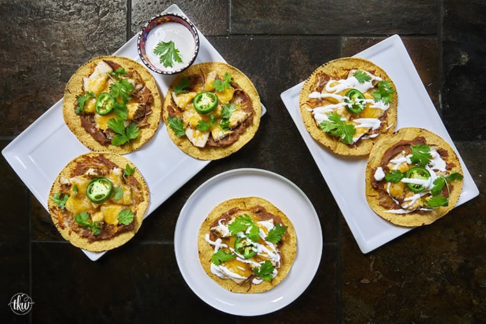 The crunch you've been craving! These Loaded Chicken and Bean Tostadas feature golden-baked shells, seasoned refried beans, juicy chicken, bubbly Mexican cheese, and spicy jalapeños. Finished with a cool sour cream sauce and fresh cilantro for that perfect creamy-meets-crunchy bite. If you love tacos, you have to try this 30-minute twist! #ChickenTostadas #30MinuteMeals #EasyMexicanRecipes #WeeknightDinnerIdeas #BudgetFriendlyCooking