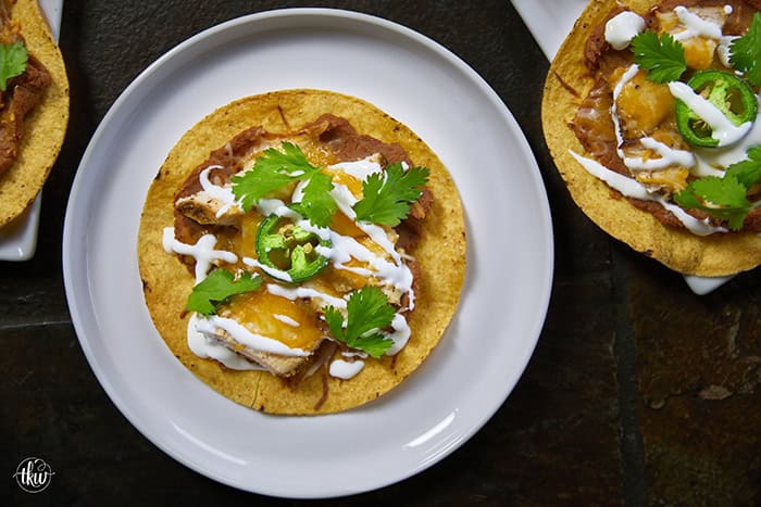 The crunch you've been craving! These Loaded Chicken and Bean Tostadas feature golden-baked shells, seasoned refried beans, juicy chicken, bubbly Mexican cheese, and spicy jalapeños. Finished with a cool sour cream sauce and fresh cilantro for that perfect creamy-meets-crunchy bite. If you love tacos, you have to try this 30-minute twist! #ChickenTostadas #30MinuteMeals #EasyMexicanRecipes #WeeknightDinnerIdeas #BudgetFriendlyCooking
