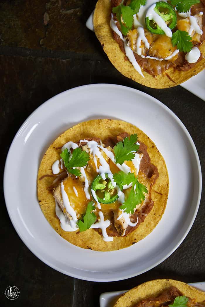 The crunch you've been craving! These Loaded Chicken and Bean Tostadas feature golden-baked shells, seasoned refried beans, juicy chicken, bubbly Mexican cheese, and spicy jalapeños. Finished with a cool sour cream sauce and fresh cilantro for that perfect creamy-meets-crunchy bite. If you love tacos, you have to try this 30-minute twist! #ChickenTostadas #30MinuteMeals #EasyMexicanRecipes #WeeknightDinnerIdeas #BudgetFriendlyCooking