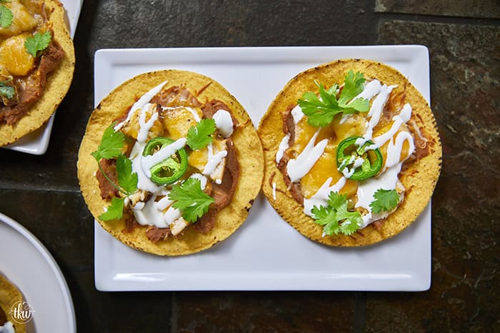 The crunch you've been craving! These Loaded Chicken and Bean Tostadas feature golden-baked shells, seasoned refried beans, juicy chicken, bubbly Mexican cheese, and spicy jalapeños. Finished with a cool sour cream sauce and fresh cilantro for that perfect creamy-meets-crunchy bite. If you love tacos, you have to try this 30-minute twist! #ChickenTostadas #30MinuteMeals #EasyMexicanRecipes #WeeknightDinnerIdeas #BudgetFriendlyCooking