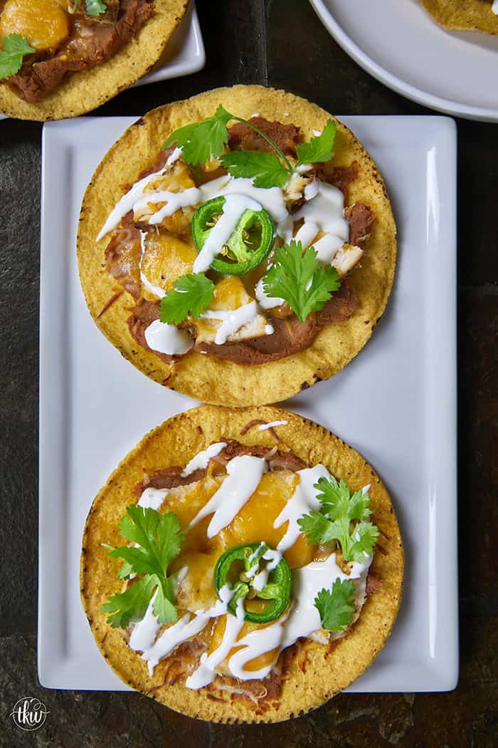 The crunch you've been craving! These Loaded Chicken and Bean Tostadas feature golden-baked shells, seasoned refried beans, juicy chicken, bubbly Mexican cheese, and spicy jalapeños. Finished with a cool sour cream sauce and fresh cilantro for that perfect creamy-meets-crunchy bite. If you love tacos, you have to try this 30-minute twist! #ChickenTostadas #30MinuteMeals #EasyMexicanRecipes #WeeknightDinnerIdeas #BudgetFriendlyCooking