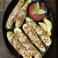 These easy zucchini strips are topped with a toasted Parmesan herb crust! Made in the oven or air fryer, they are the perfect light summer side dish or appetizer to pair with your favorite dipping sauce. #easyzucchini #zucchinistrips #bakedzucchini