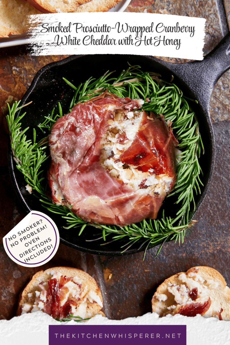 Smoked Prosciutto-Wrapped Cranberry White Cheddar Cheese drizzled with hot honey and fresh rosemary on a serving board with crostini.
