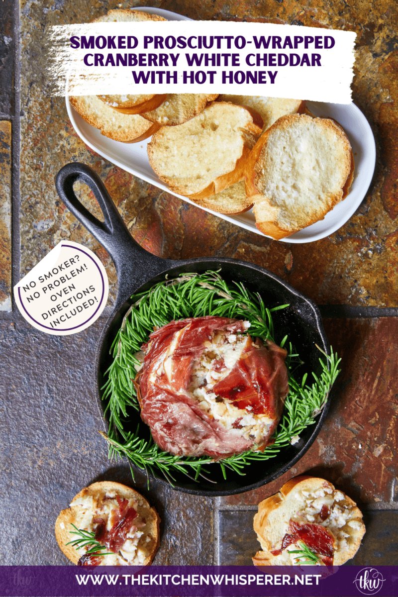 Smoked Prosciutto-Wrapped Cranberry White Cheddar Cheese drizzled with hot honey and fresh rosemary on a serving board with crostini.